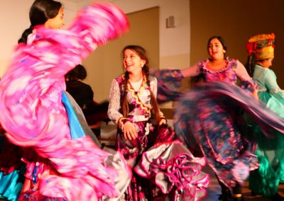 Zdjęcie przedstawia wirujące w tańcu, roześmiane dziewczynki w barwnych tradycyjnych romskich sukniach.