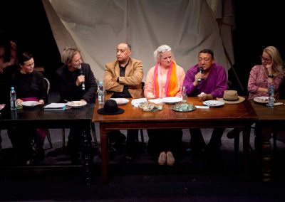 Zdjęcie przedstawia 6 osób, zamyślonych i zasłuchanych kobiet i mężczyzn siedzących przy konferencyjnym stole. Niektórzy trzymają mikrofony, jeden z mężczyzn się do niego wypowiada. Przed nimi stoją talerzyki i butelki po wodzie.