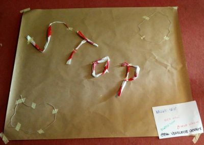 Zdjęcie przedstawia szary papier na którym z biało czerwonej taśmy ułożono napis stop. W prawym dolnym rogu mała biała karteczka z odręcznymi napisami w języku polskim i niemieckim.