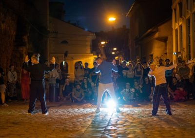 Na nocnej brukowej ulicy oświetlonej reflektorem dziewczyna i dwóch chłopaków wykonują układ taneczny. Stoją zwróceni do publiczności, twarze mają skierowane w lewą stronę, a dłonie wystawione przed siebie w geście stop. Są ubrani na sportowo.