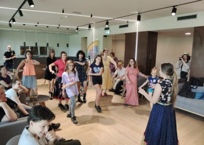 Dziesięć uśmiechniętych kobiet i dziewczynek uczy się tańca w sali. Powtarzają ruchy szatynki ubranej w romską sukienkę. Obserwują je siedzący na kanapach chłopcy, mężczyźni i kobiety.